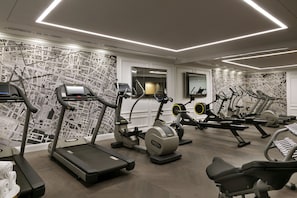 Un gimnasio con cintas de correr, elípticas y un espejo grande.