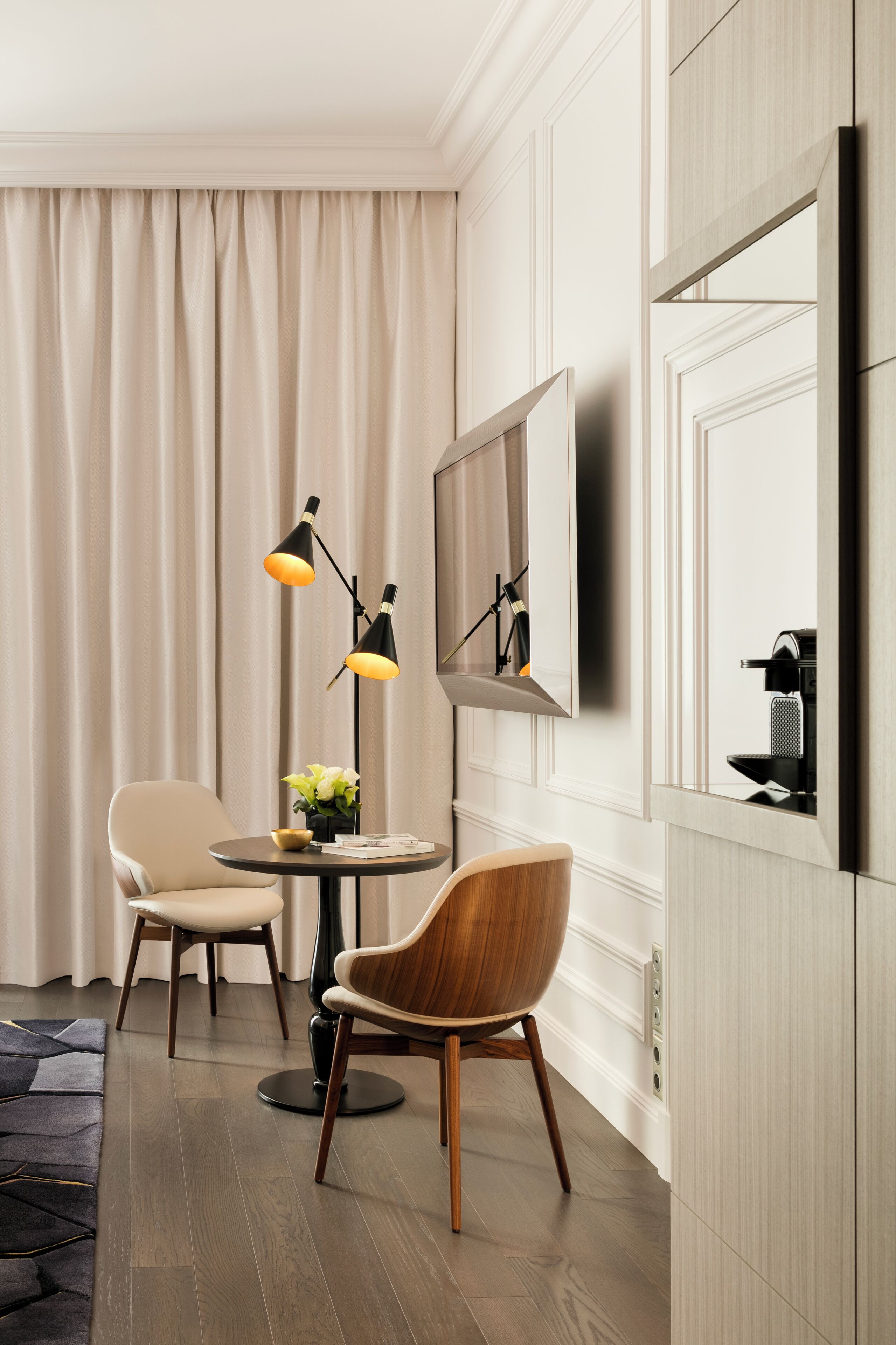 A modern room with a round table, two chairs, a floor lamp, a television, and a coffee machine.
