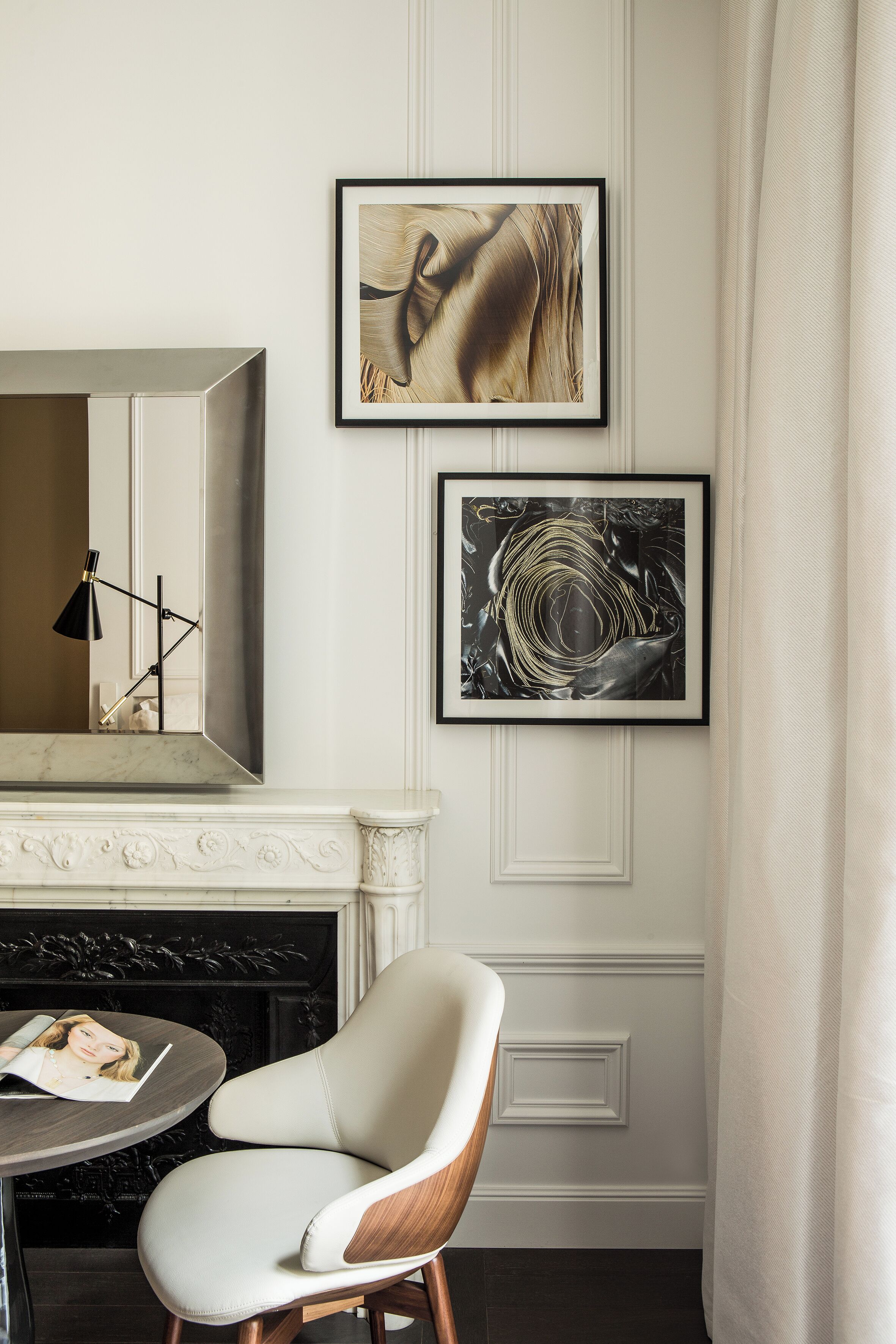 Una habitación moderna con chimenea, una silla blanca y dos obras de arte enmarcadas en la pared.