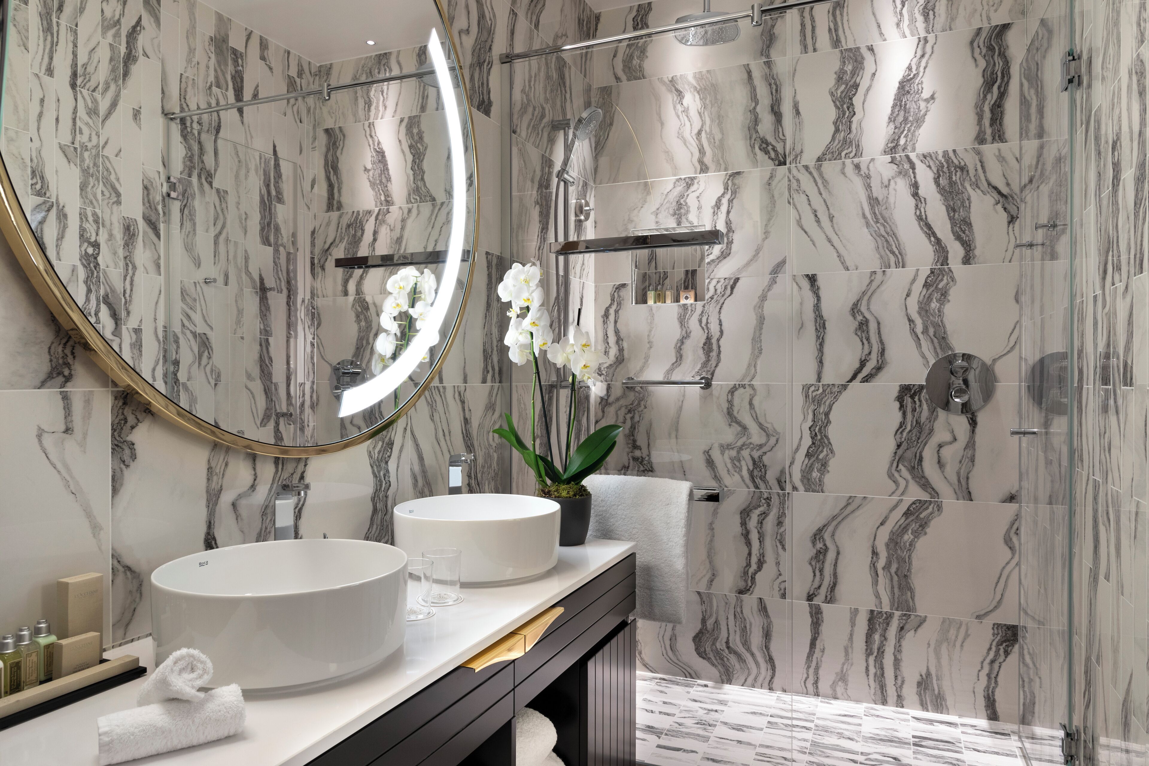 A bathroom with marble walls, a round sink, a mirror, a towel, and a potted plant.
