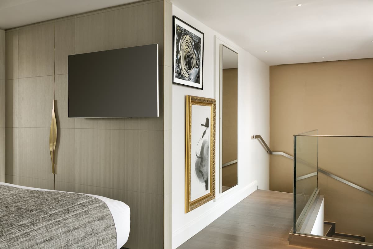 Een moderne hotelkamer met een groot bed, een flatscreen televisie aan de muur en een trap met glazen balustrades.