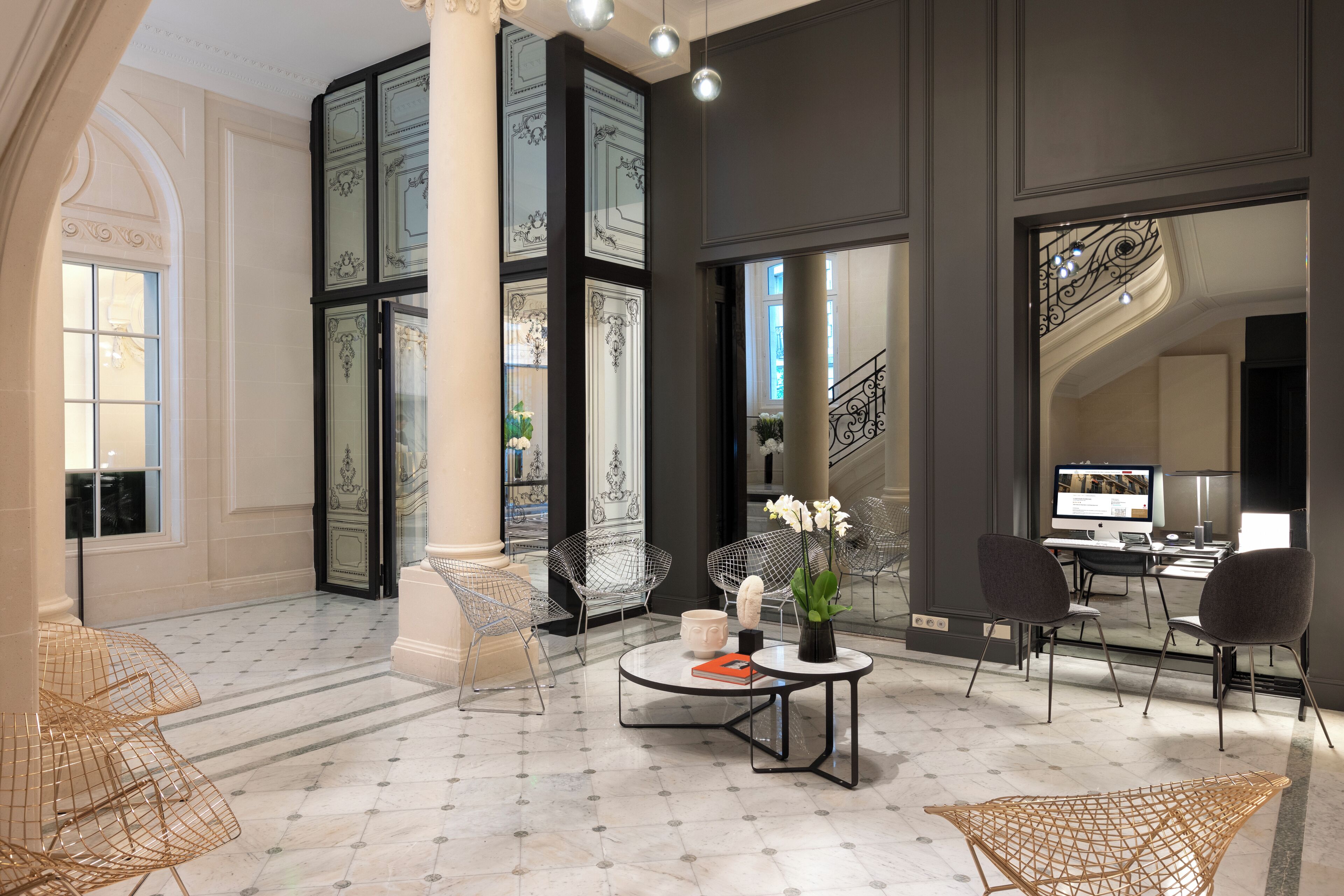 A spacious lobby with a marble floor, a central seating area with chairs and a table, and a staircase with ornate railings.