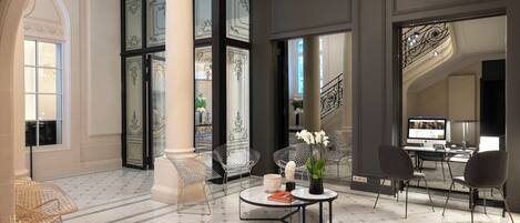 A spacious lobby with a marble floor, a central seating area with chairs and a table, and a staircase with ornate railings.
