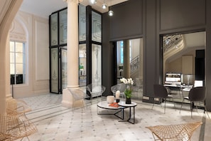Un hall d’entrée spacieux doté d’un sol en marbre, un espace de détente central avec des fauteuils et une table, ainsi qu’un escalier orné de rampes décoratives.