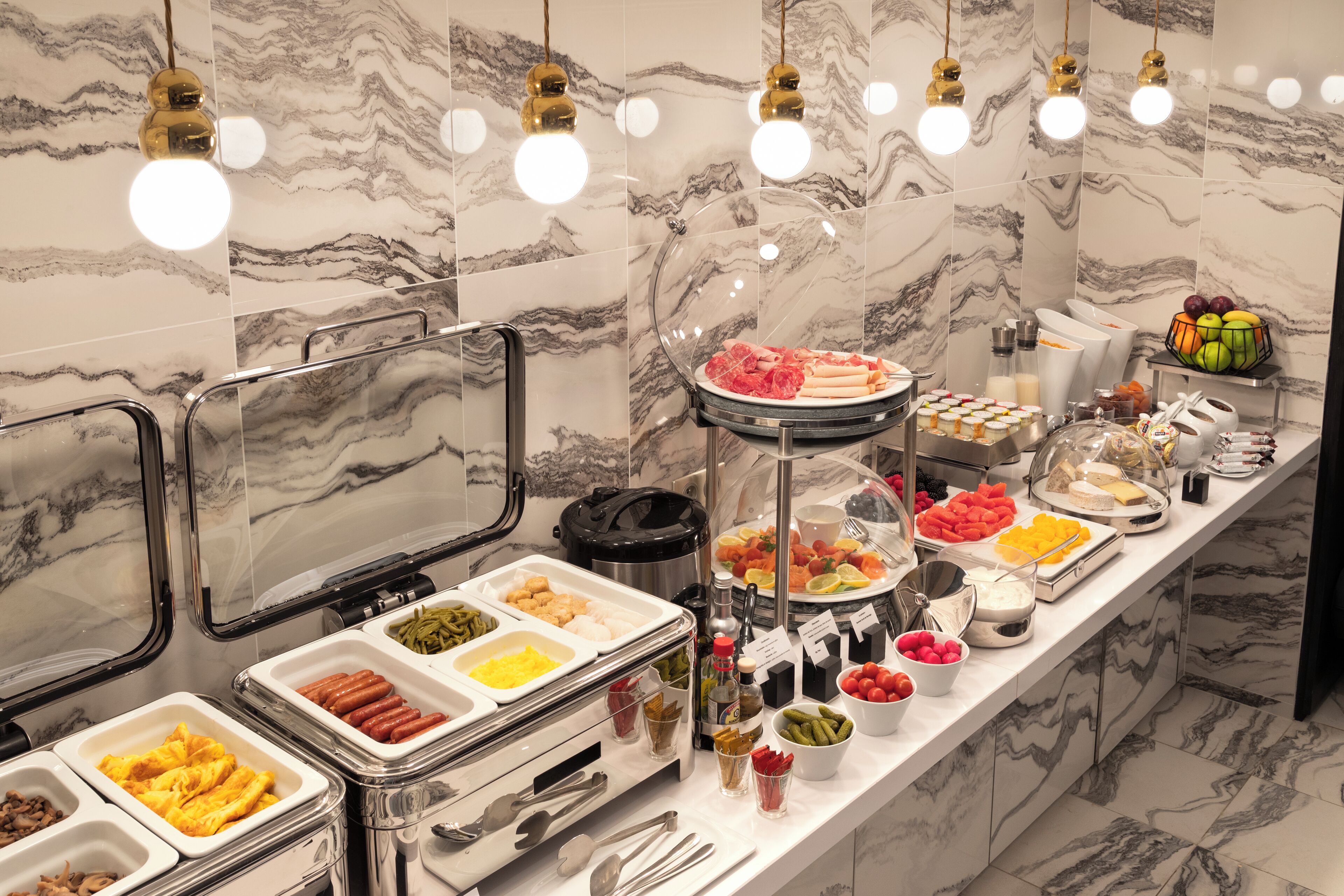 A buffet with various food options and a marble wall background.