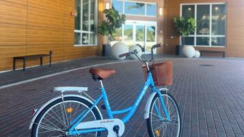 Uma bicicleta azul estacionada numa área pavimentada com tijolos, com um edifício moderno ao fundo.