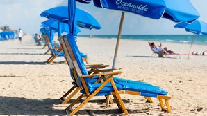 Una playa con hileras de sillas azules y sombrillas, algunas ocupadas por personas.
