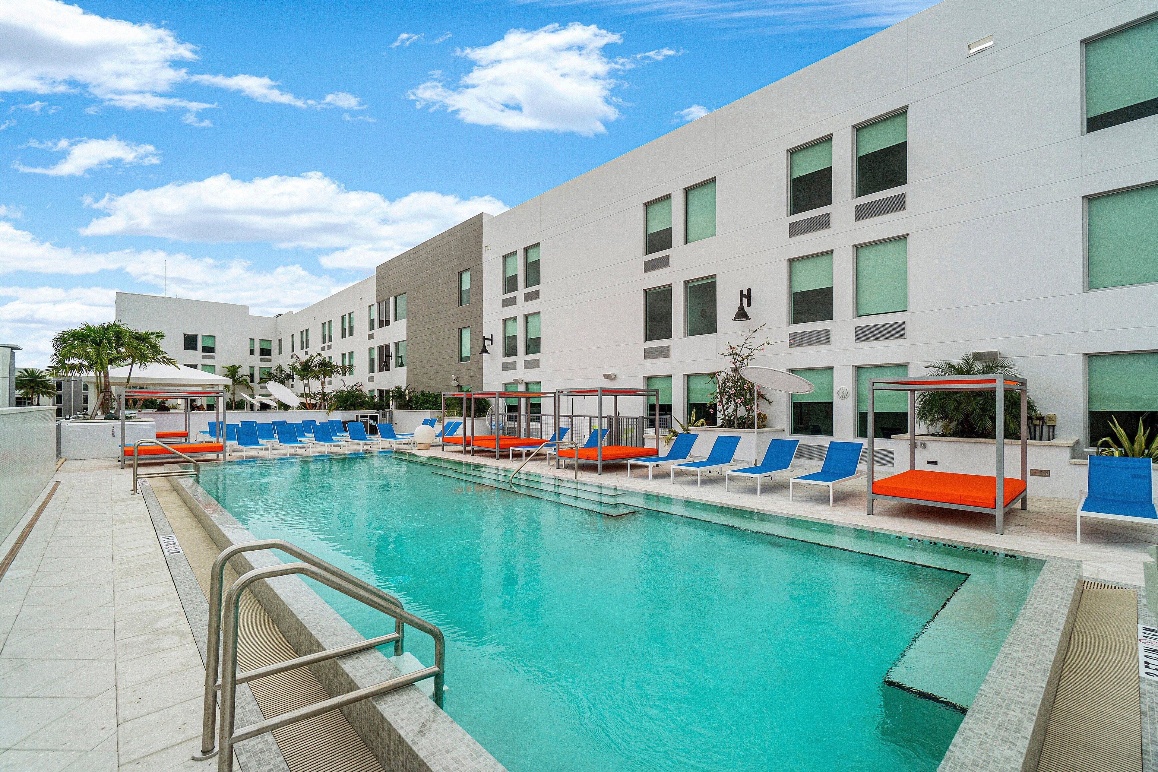 A swimming pool with lounge chairs and a modern building in the background.