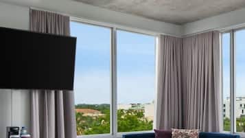 A modern hotel room with large windows, a flat-screen TV, a sofa, and a coffee machine.