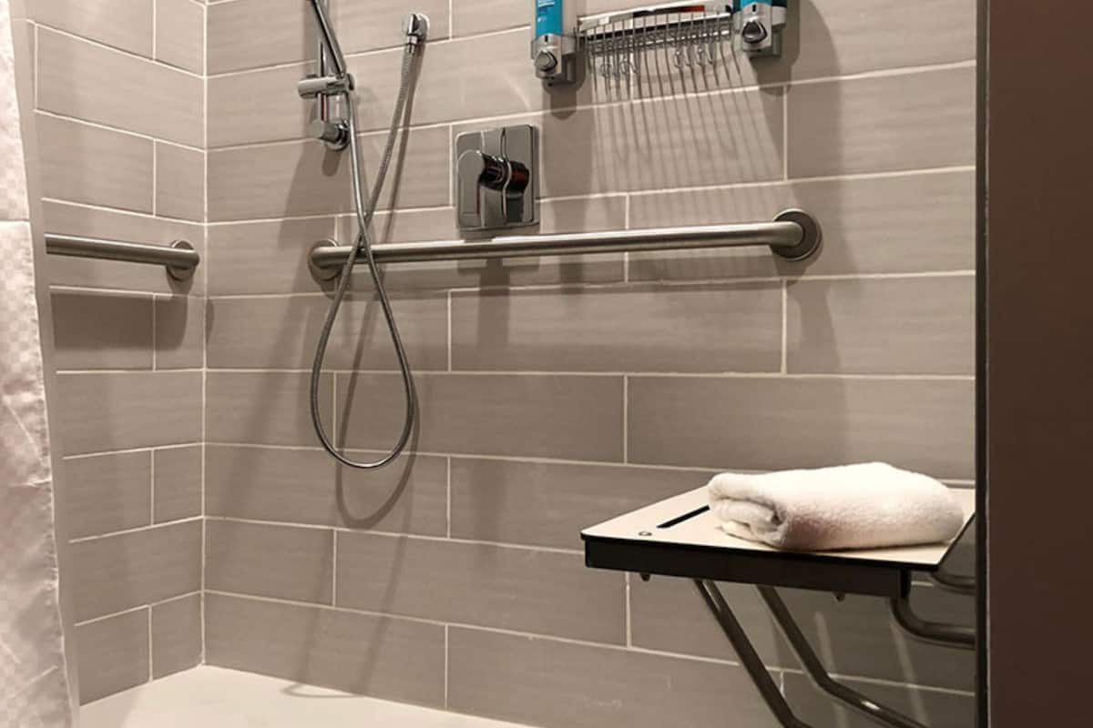 Zona de ducha con barra de apoyo, perchero y cabezal de ducha manual.