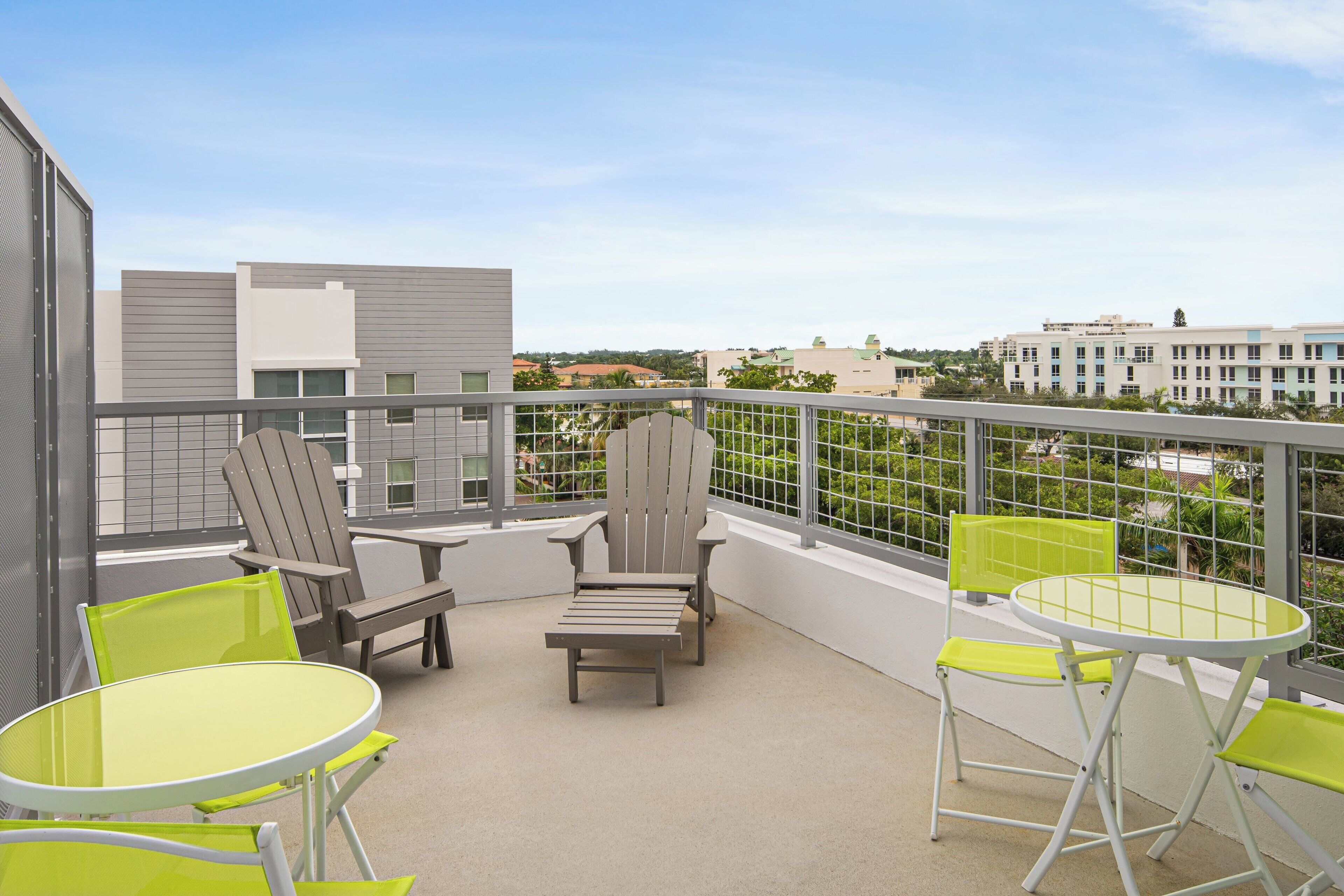 A balcony with outdoor seating, including two Adirondack chairs and two small round tables.