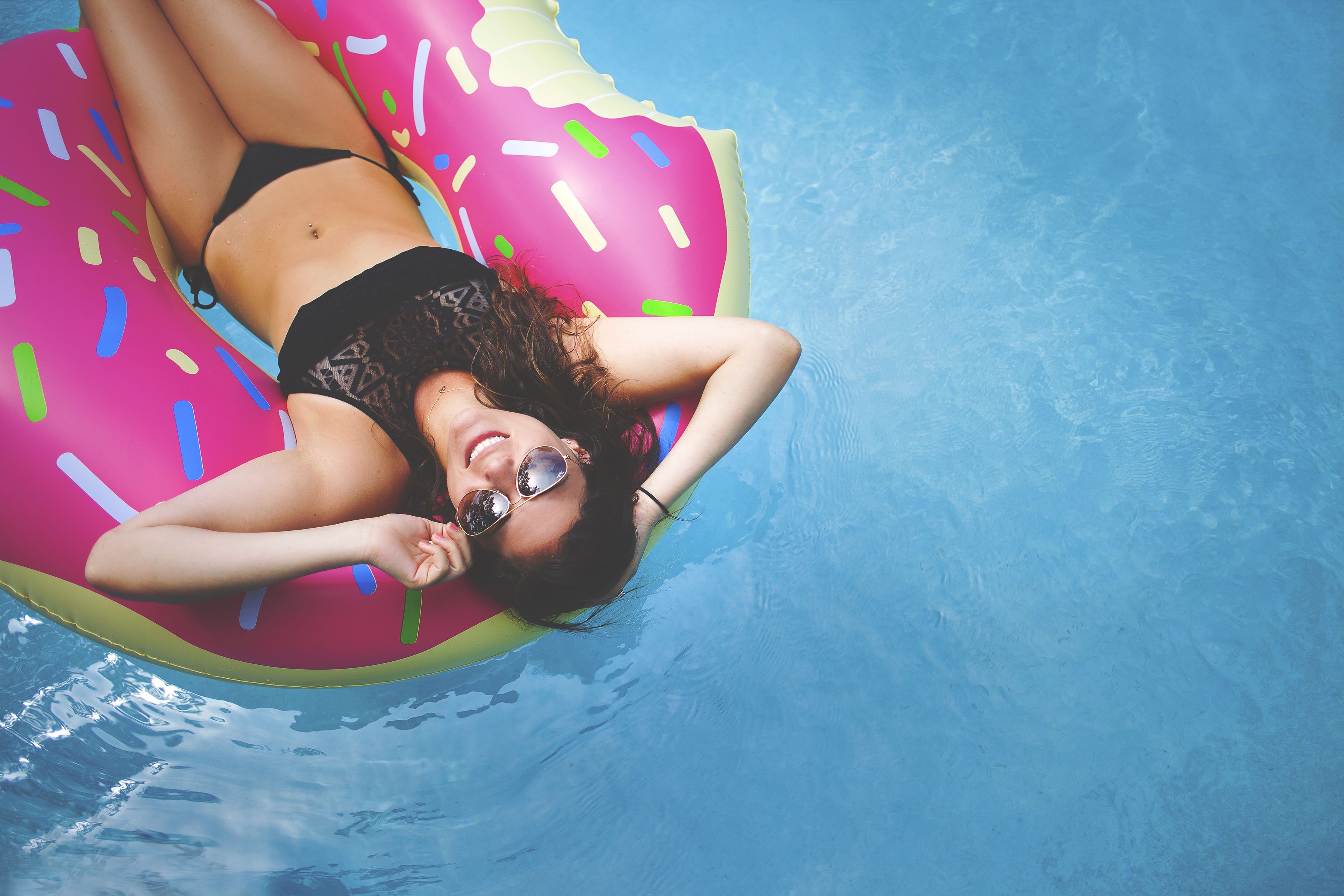 Una persona sdraiata su un cerchio galleggiante a forma di ciambella rosa in una piscina.