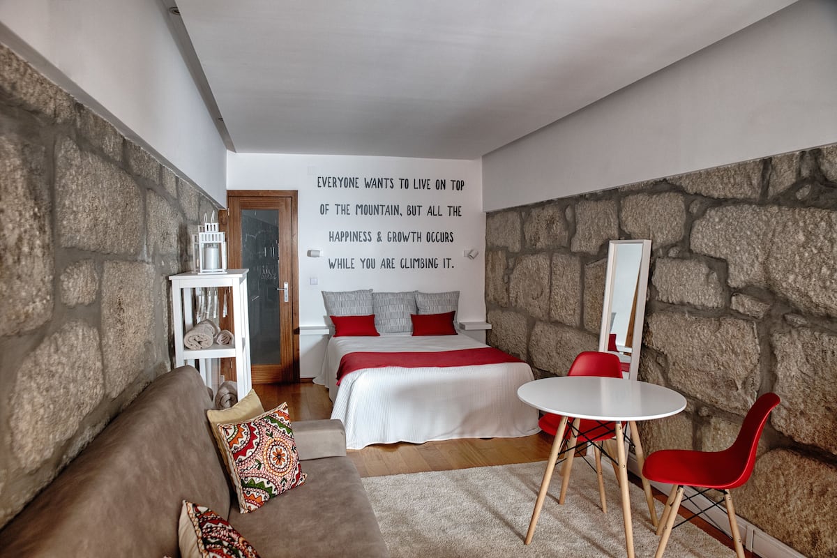 A cozy bedroom with a bed, a red chair, a small table, and a motivational quote on the wall.