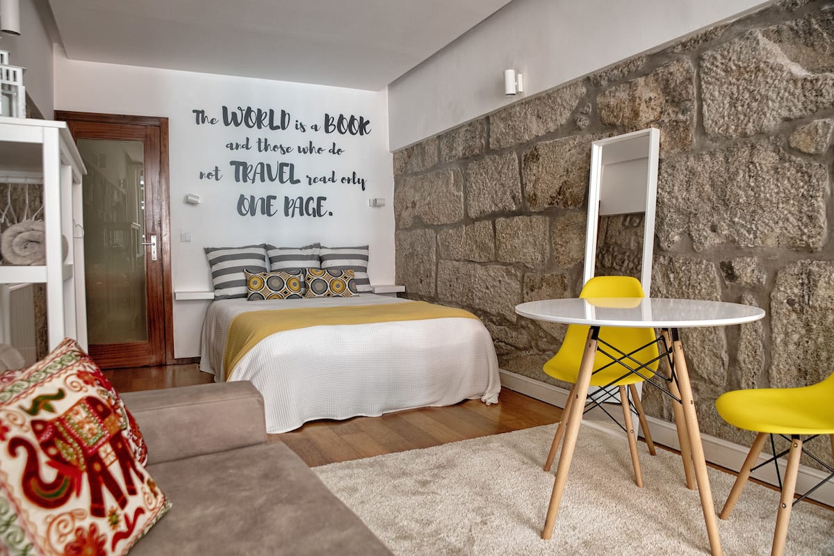 A bedroom with a bed, a bedside table, a mirror, a yellow chair, and a wall with a motivational quote.