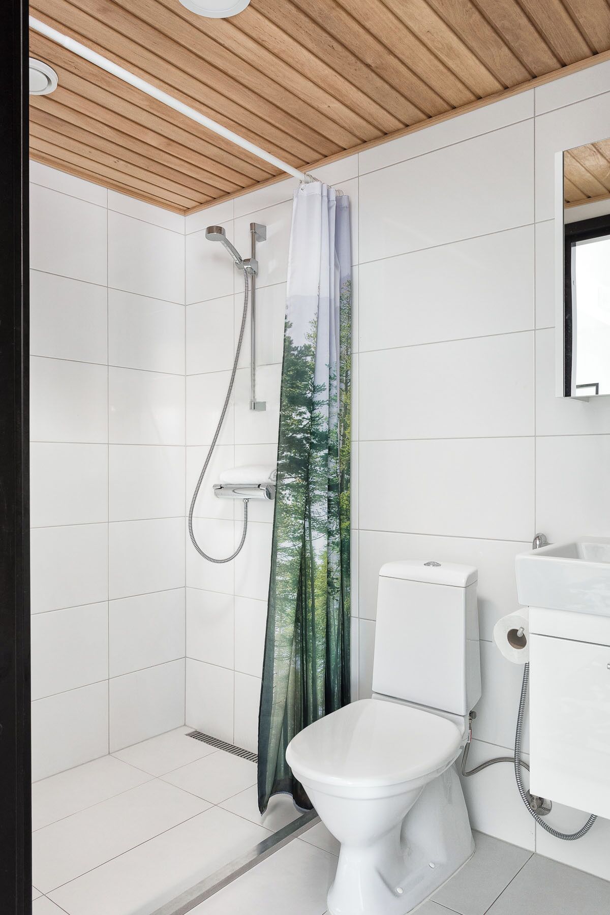 A modern bathroom with white tiles, a shower with a rain curtain, a toilet, and a sink.