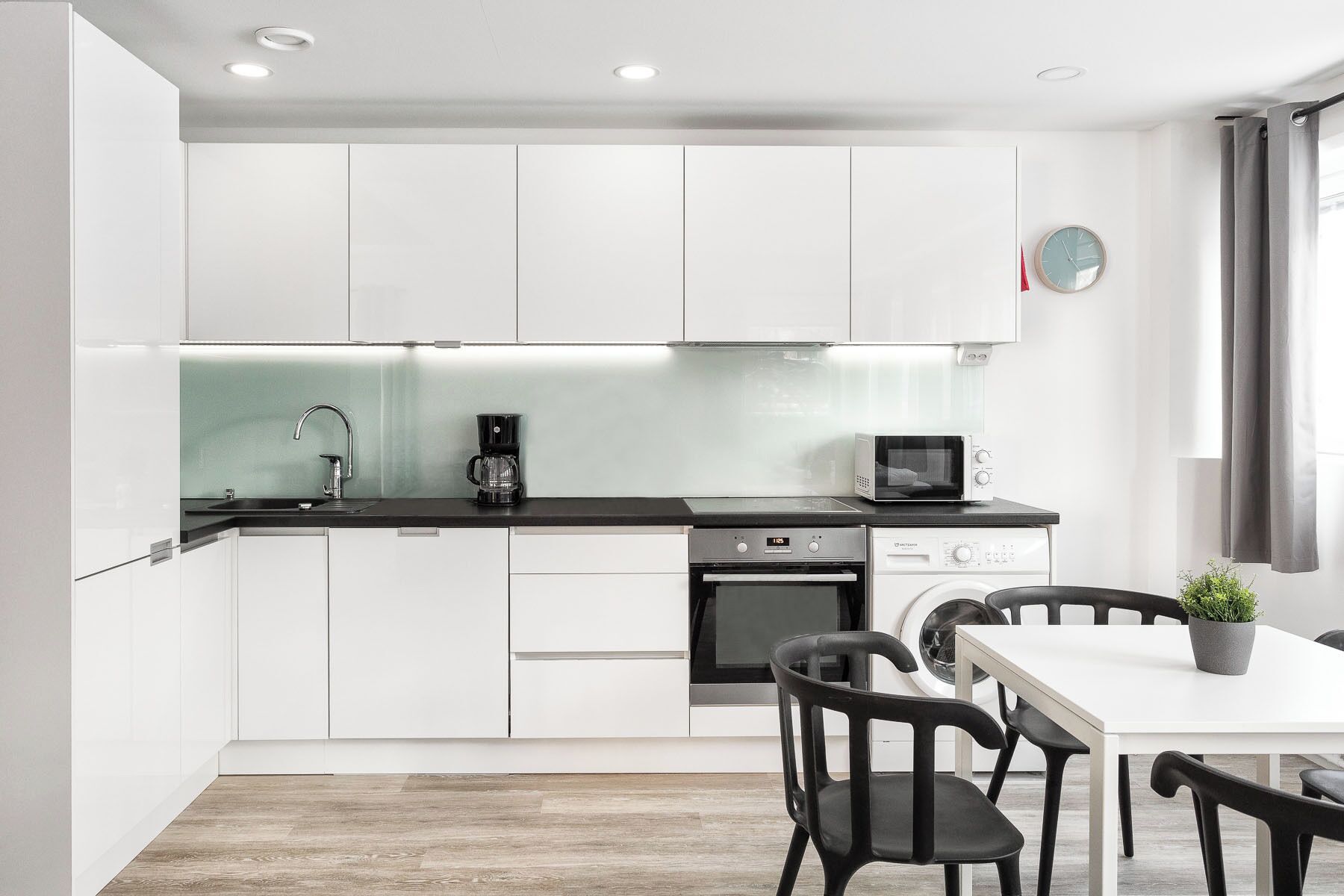 A modern kitchen with white cabinets, a black countertop, a coffee maker, a microwave, and a dining area with a table and chairs.