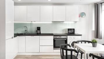 A modern kitchen with white cabinets, a black countertop, a coffee maker, a microwave, and a dining area with a table and chairs.