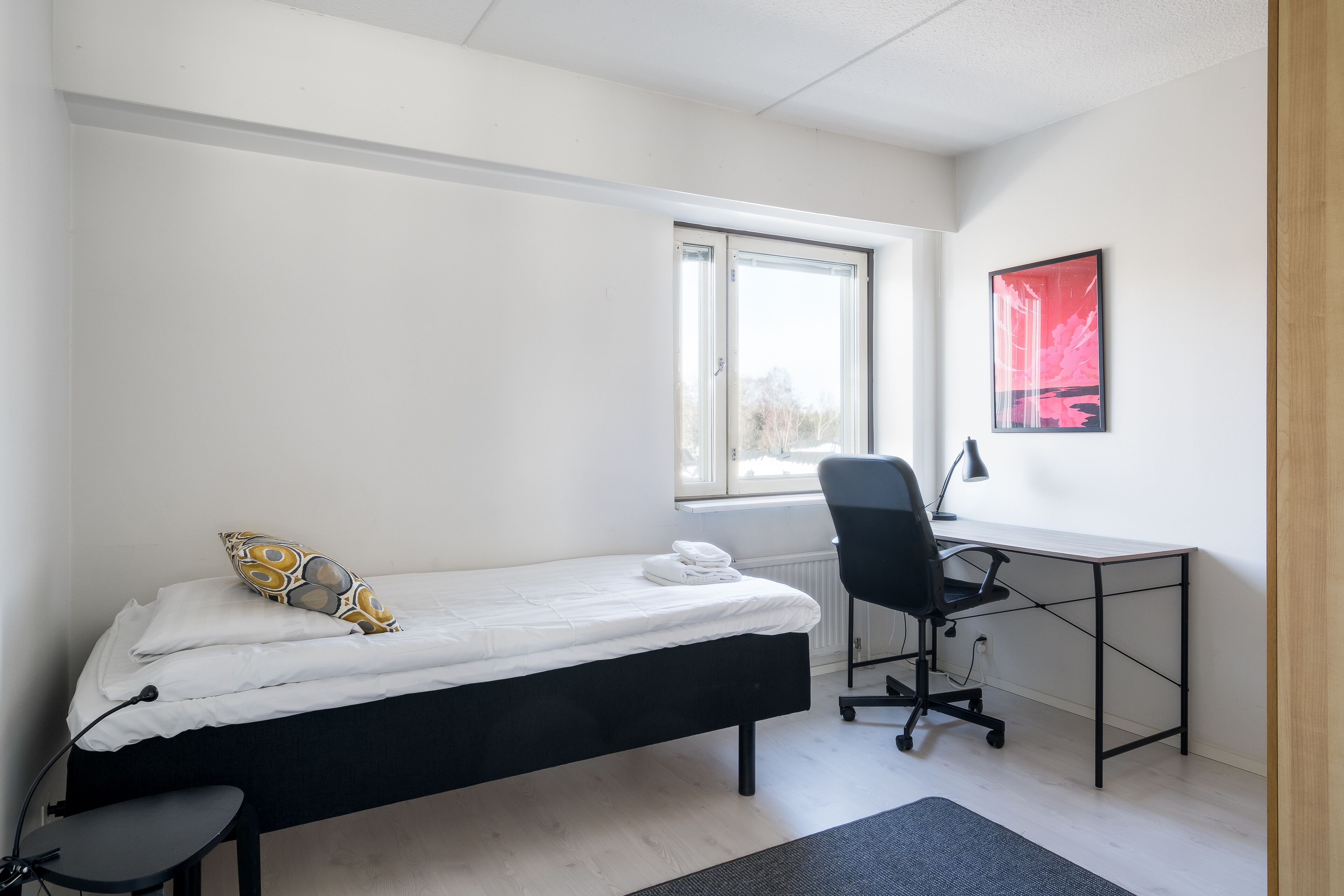 A small, clean room with a bed, a desk, and a chair.