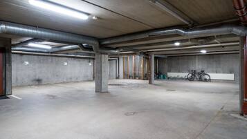 Un parcheggio sotterraneo vuoto, con pavimenti e pareti in cemento, colonne strutturali a vista e illuminazione superiore.