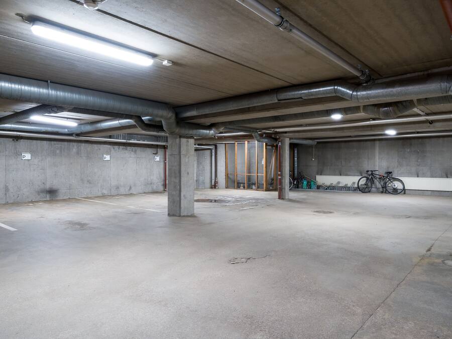 Un parking souterrain vide, avec des planchers et des murs en béton, des piliers apparents et un éclairage au plafond.