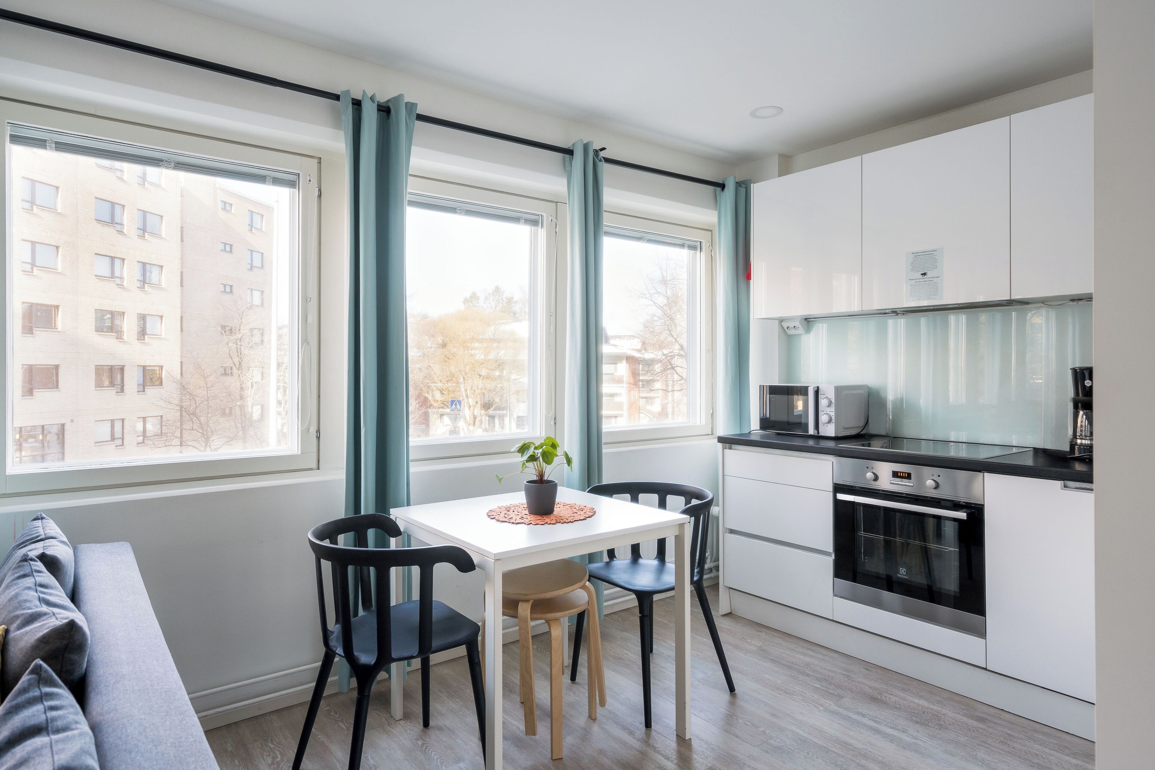A modern kitchen with a dining area, large windows, and a view of buildings outside.