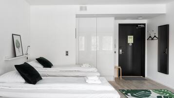Une chambre d’hôtel avec trois lits, une porte noire, un petit tabouret en bois et un tapis à motifs verts.