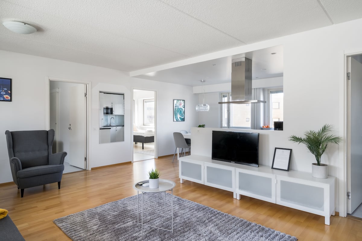 A modern living room with a grey armchair, a flat-screen TV, a white entertainment unit, and a grey rug.