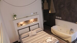 A modern bedroom with a large bed, a built-in shelf with decorative items, a bedside table, and a separate bathtub. - Gea apartment Etna (Nicolosi)