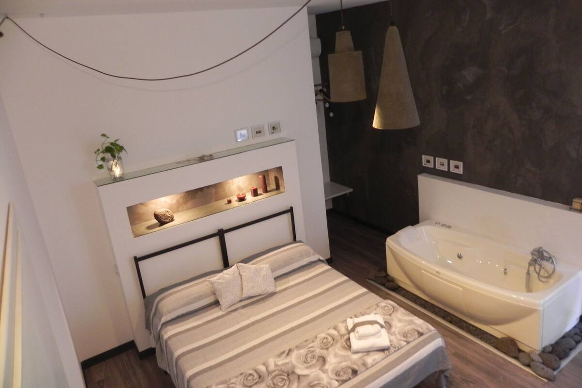 Een moderne slaapkamer met een groot bed, een inbouwkast met decoratieve objecten, een nachtkastje en een losstaande badkuip.