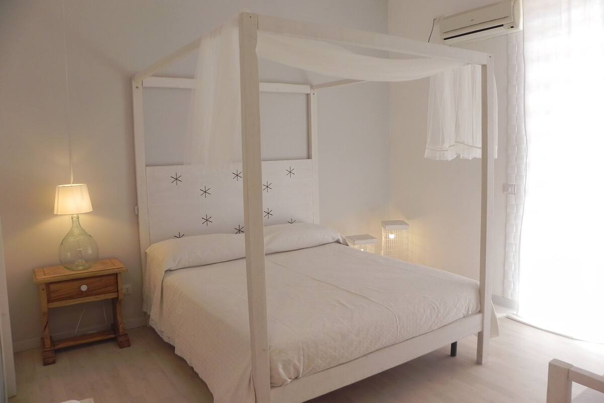 Een hemelbed met baldakijn, een nachtkastje met een lamp, en een nachtkastje met een lamp.