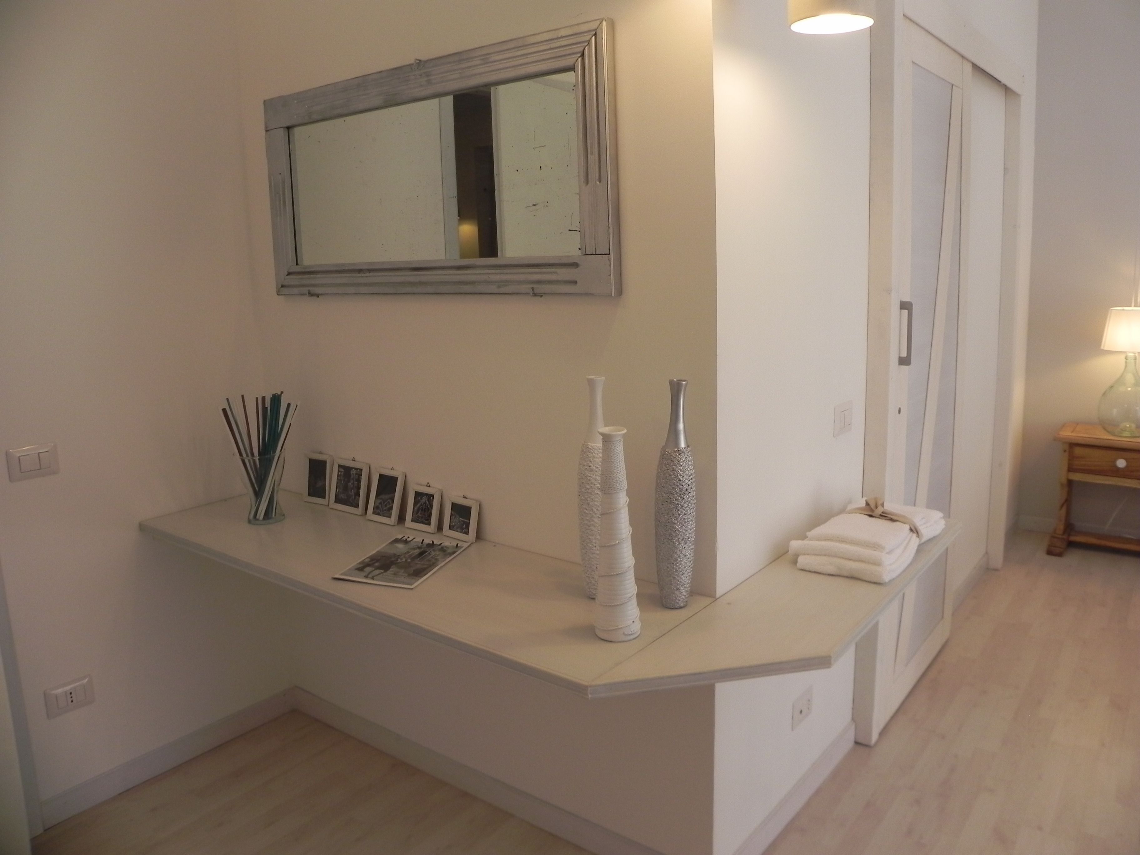 A bathroom with a white vanity, a mirror, and a small bedside table with a lamp.