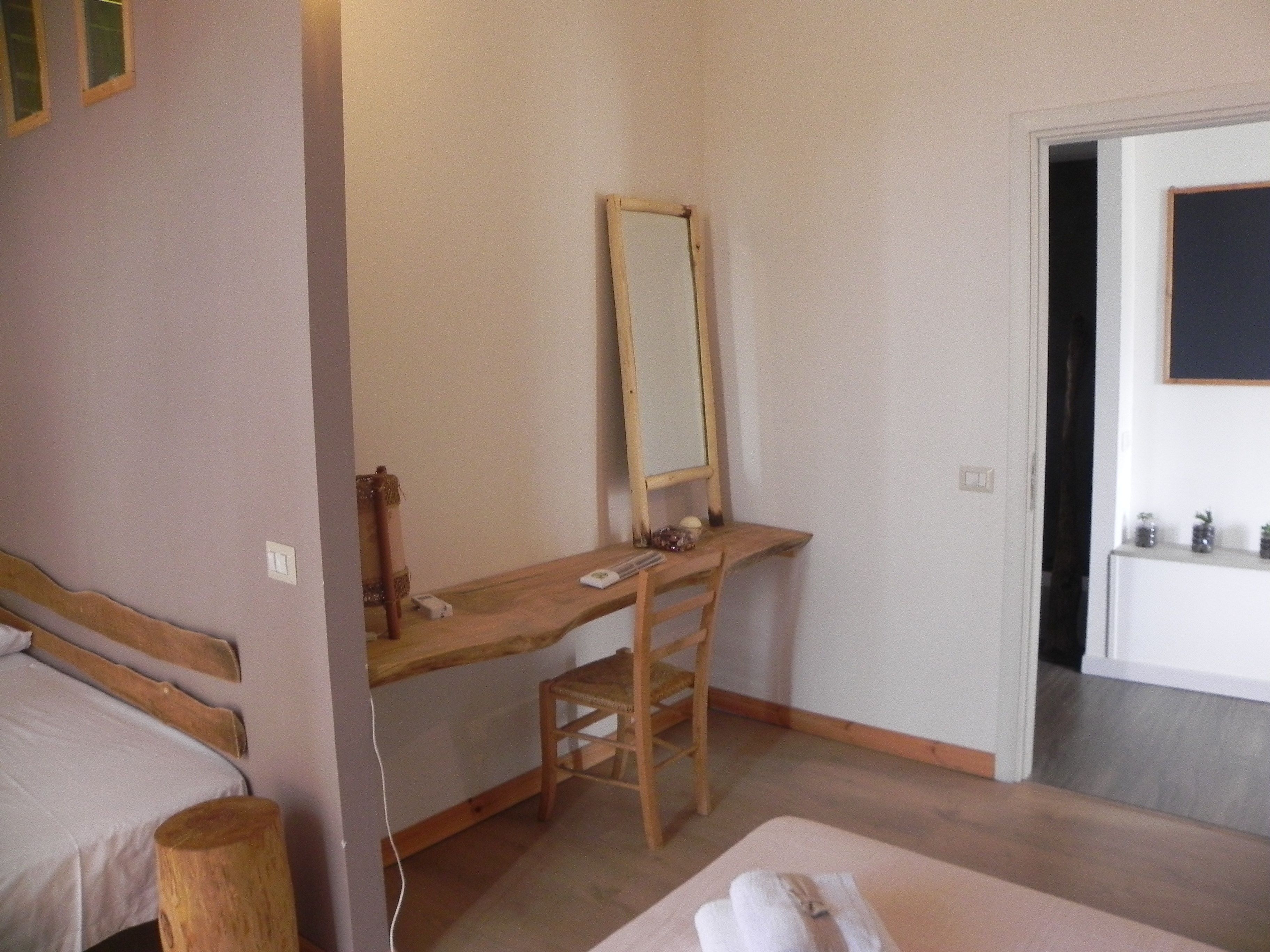 Een slaapkamer met een houten bureau, een stoel, een bed en een spiegel.
