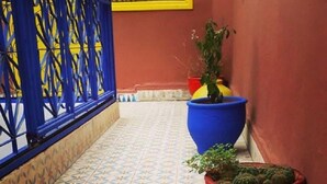 Un passadís amb rajoles, barana blava, finestra groga i plantes en testos.