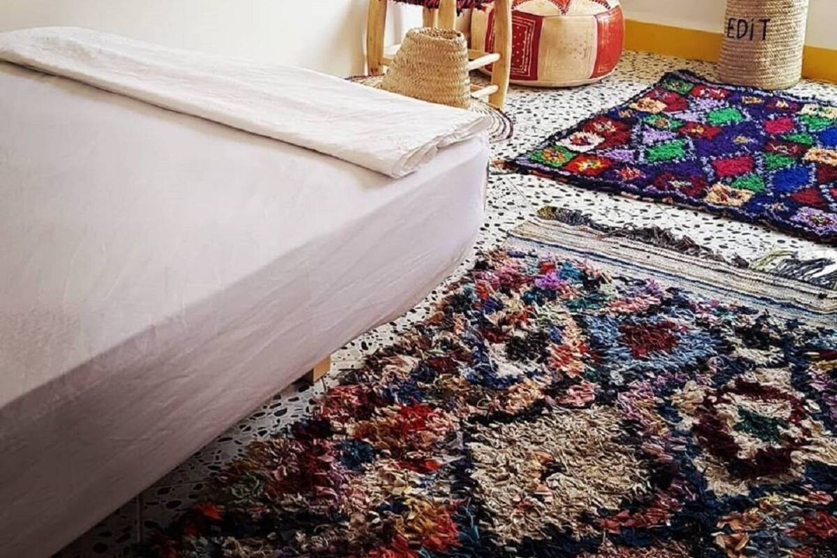Une chambre à coucher avec un lit, un tapis coloré et un petit tabouret en bois.
