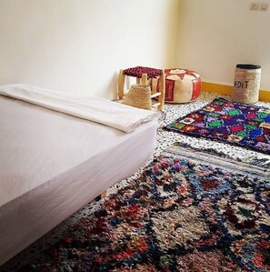 A bedroom with a bed, a colorful rug, and a small wooden stool. - Mosaic Hostel (Marrakech)