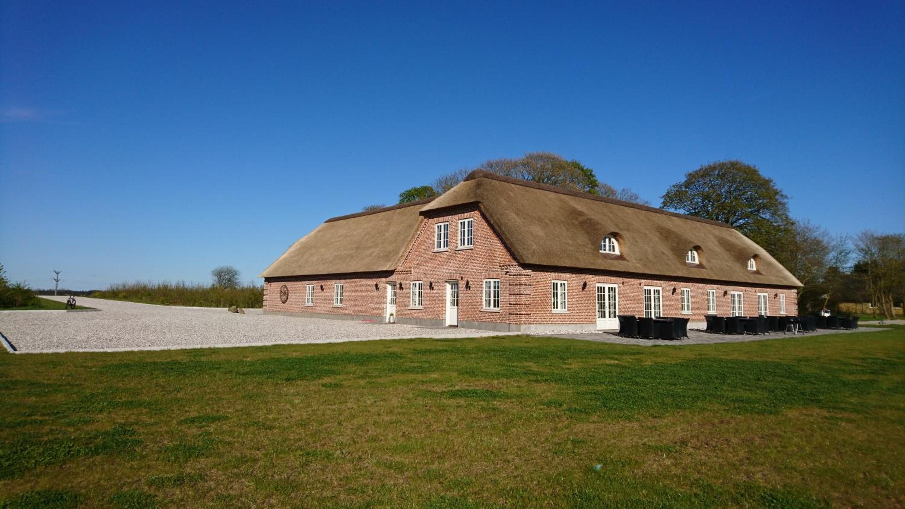 A large brick building with a thatched roof, a gravel driveway, and a grassy lawn.