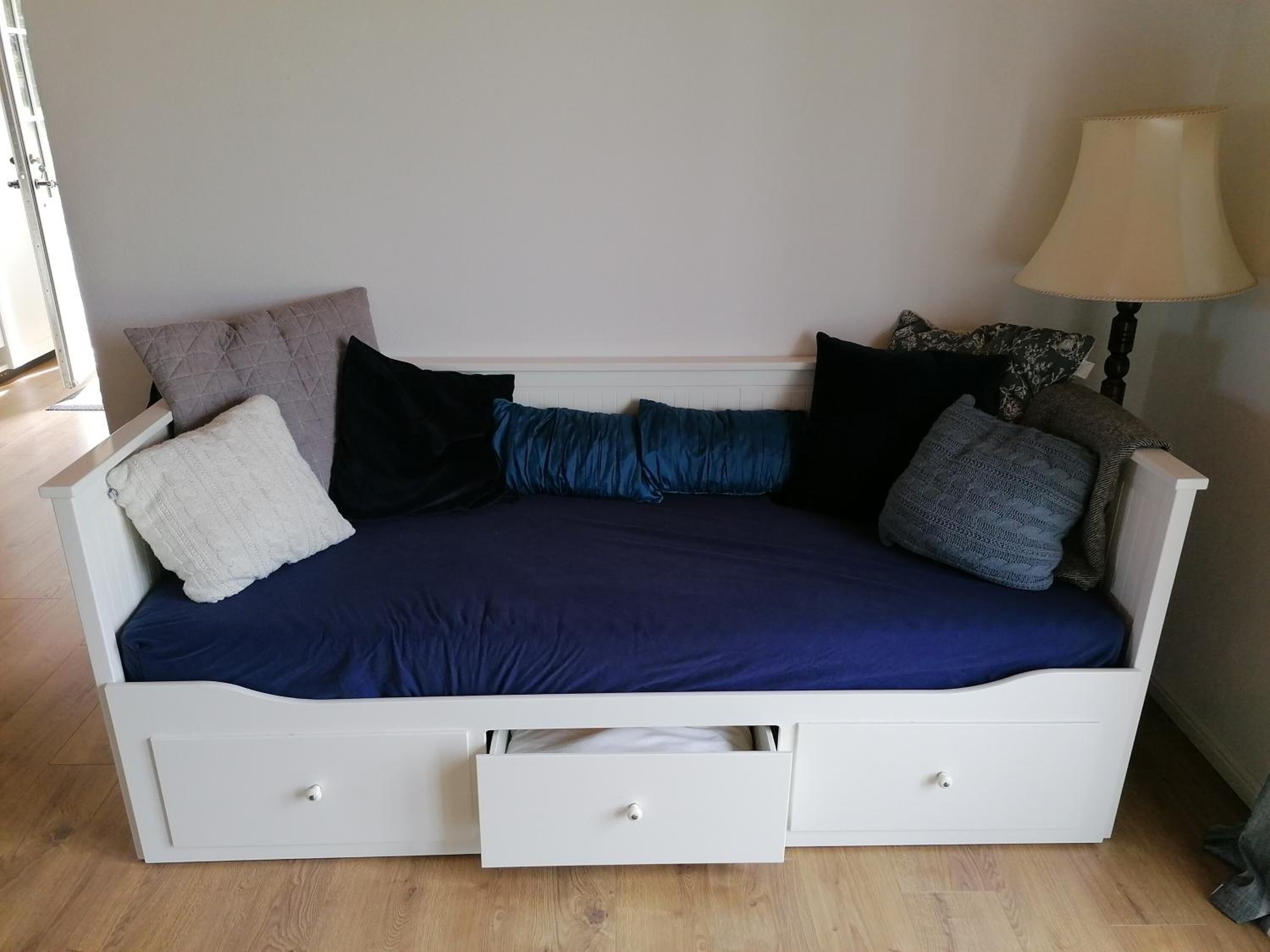 Un canapé-lit blanc avec un revêtement bleu, plusieurs coussins et deux tiroirs.