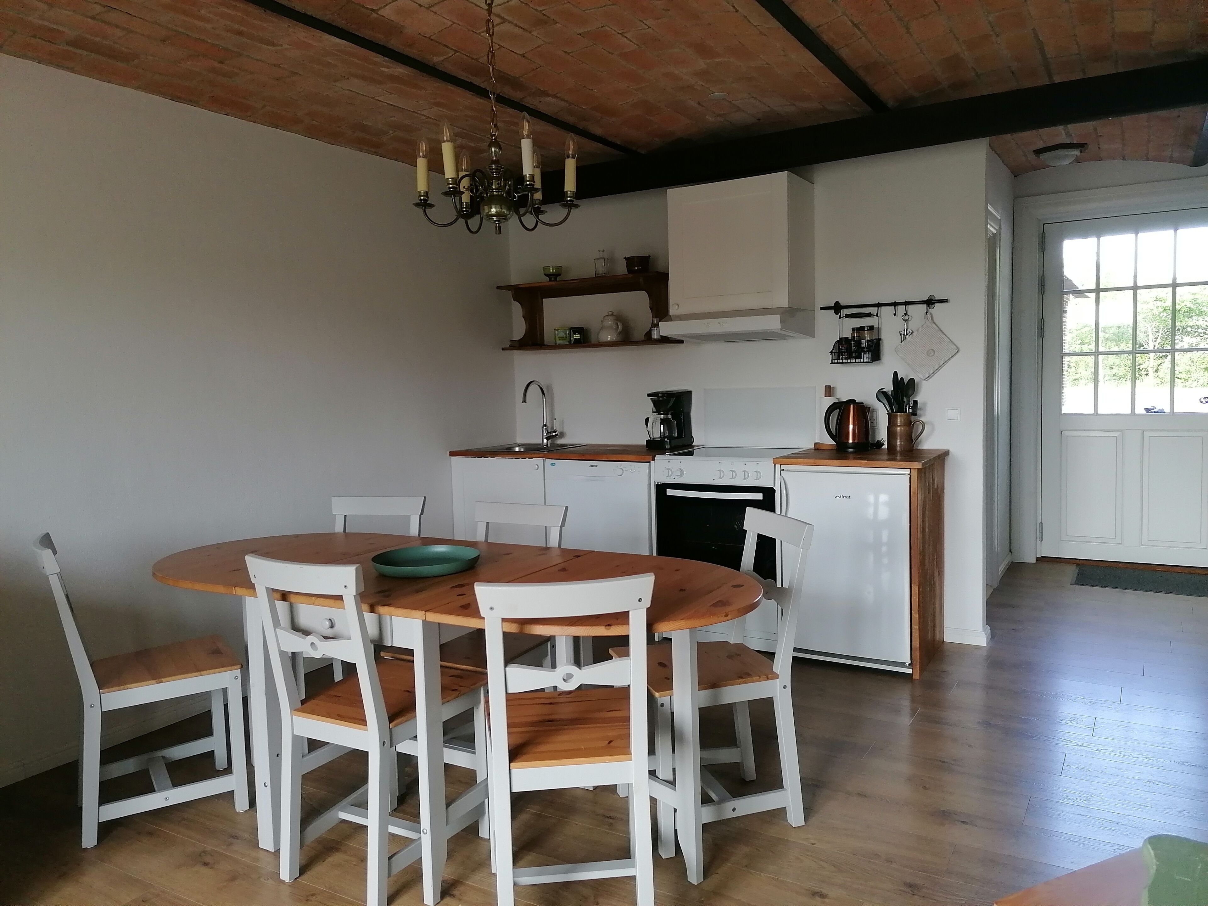 A kitchen with a round wooden table, white chairs, a white dishwasher, a white oven, and a coffee maker.