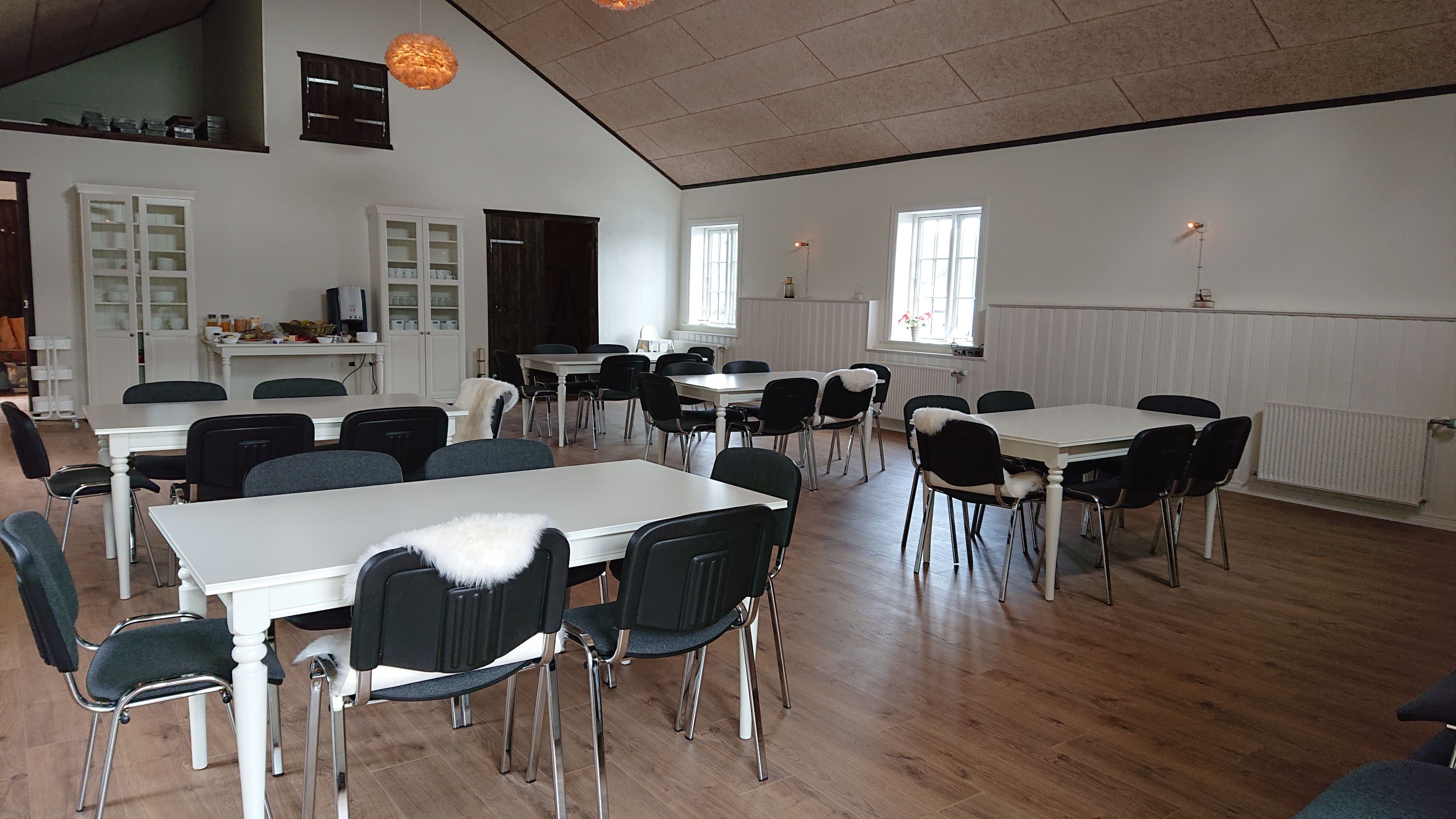 A spacious dining area with multiple tables and chairs, white walls, and large windows allowing natural light.