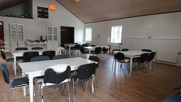 A spacious dining area with multiple tables and chairs, white walls, and large windows allowing natural light.