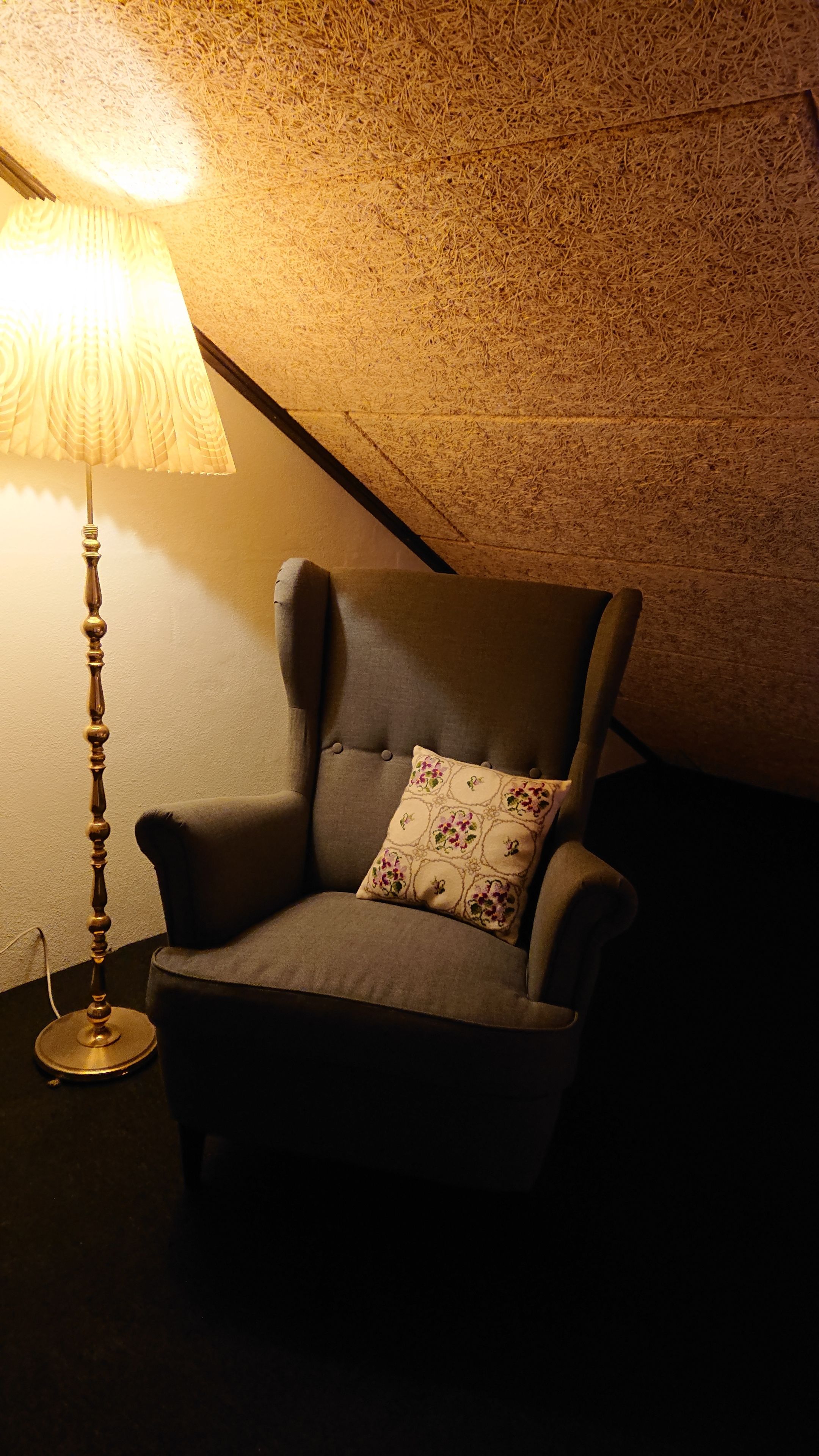 A cozy room with a chair, a lamp, and a textured ceiling.