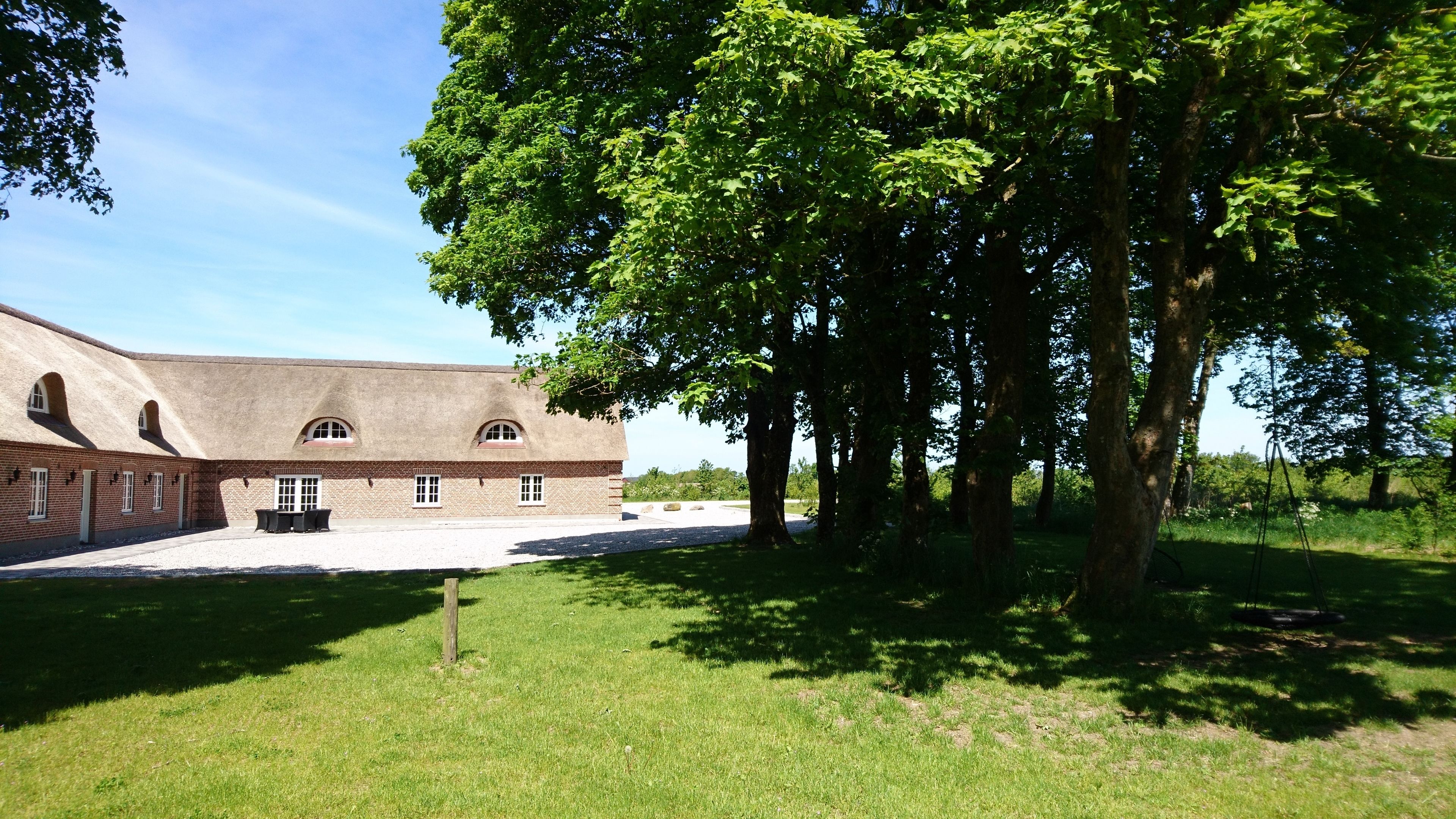 A building with a brick exterior and a thatched roof, surrounded by a grassy area and trees.