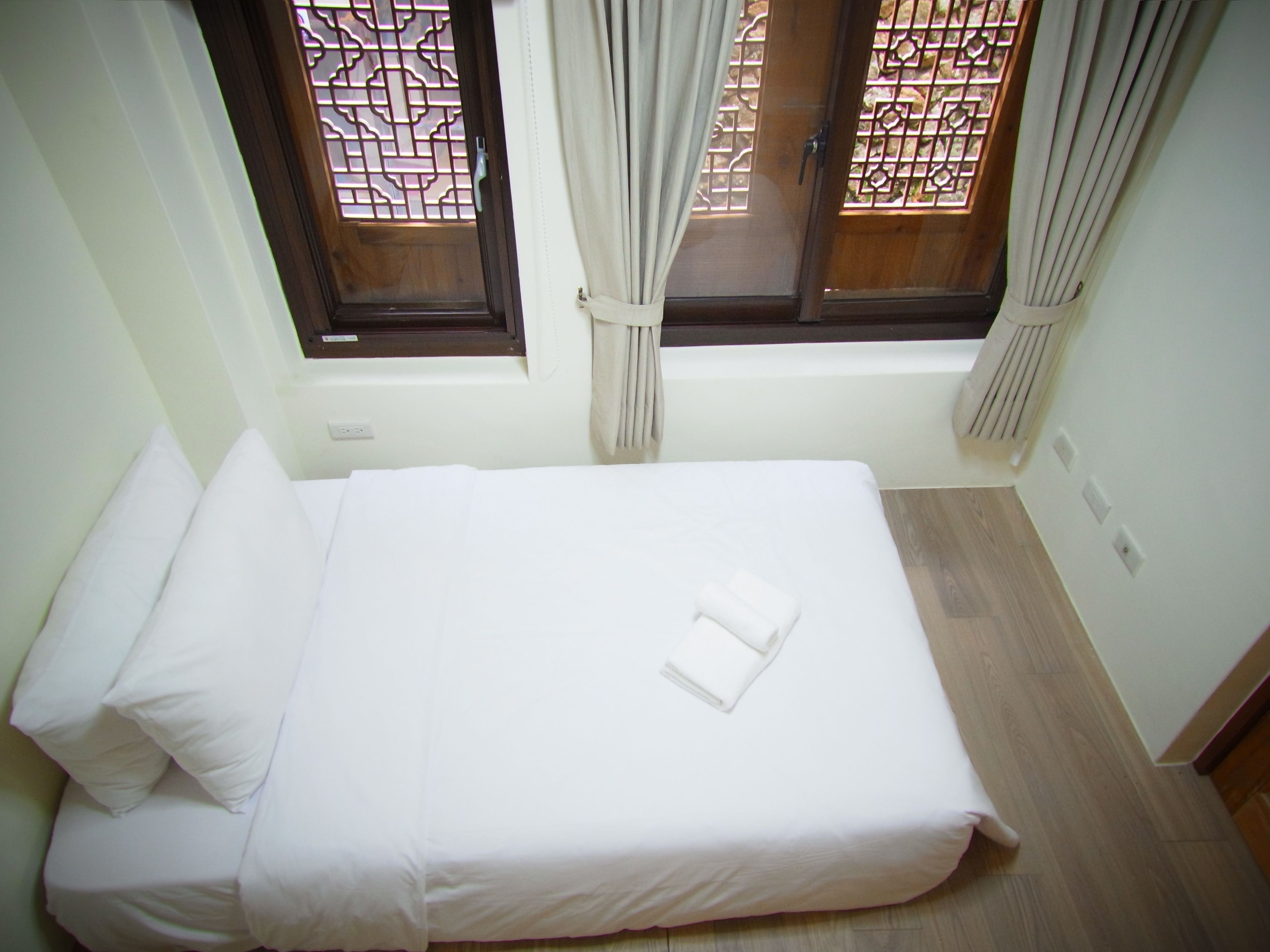 A neatly made bed in a room with two windows, each with a wooden frame and decorative metal grilles.
