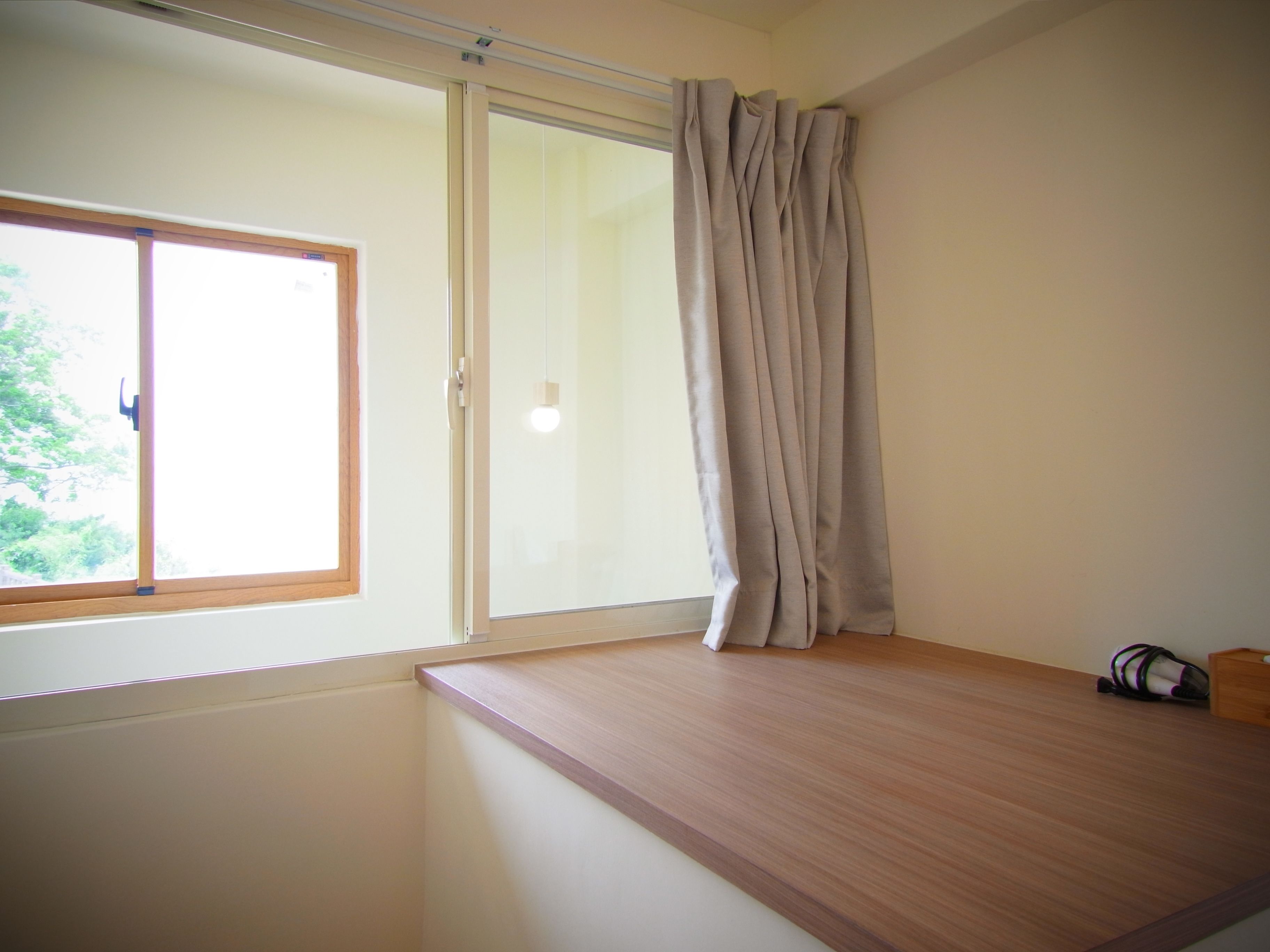 Una habitación con un ventanal grande, un escritorio de madera y una cortina.