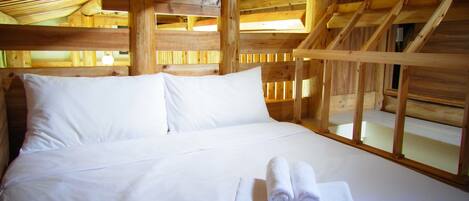 Quarto de cabana de madeira com cama, almofadas e toalhas enroladas.