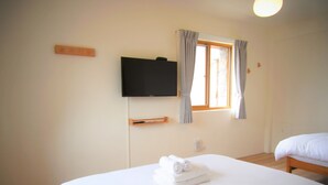 Habitació d'hotel amb llit, televisió penjada a la paret, finestra amb cortines i una taula de nit.