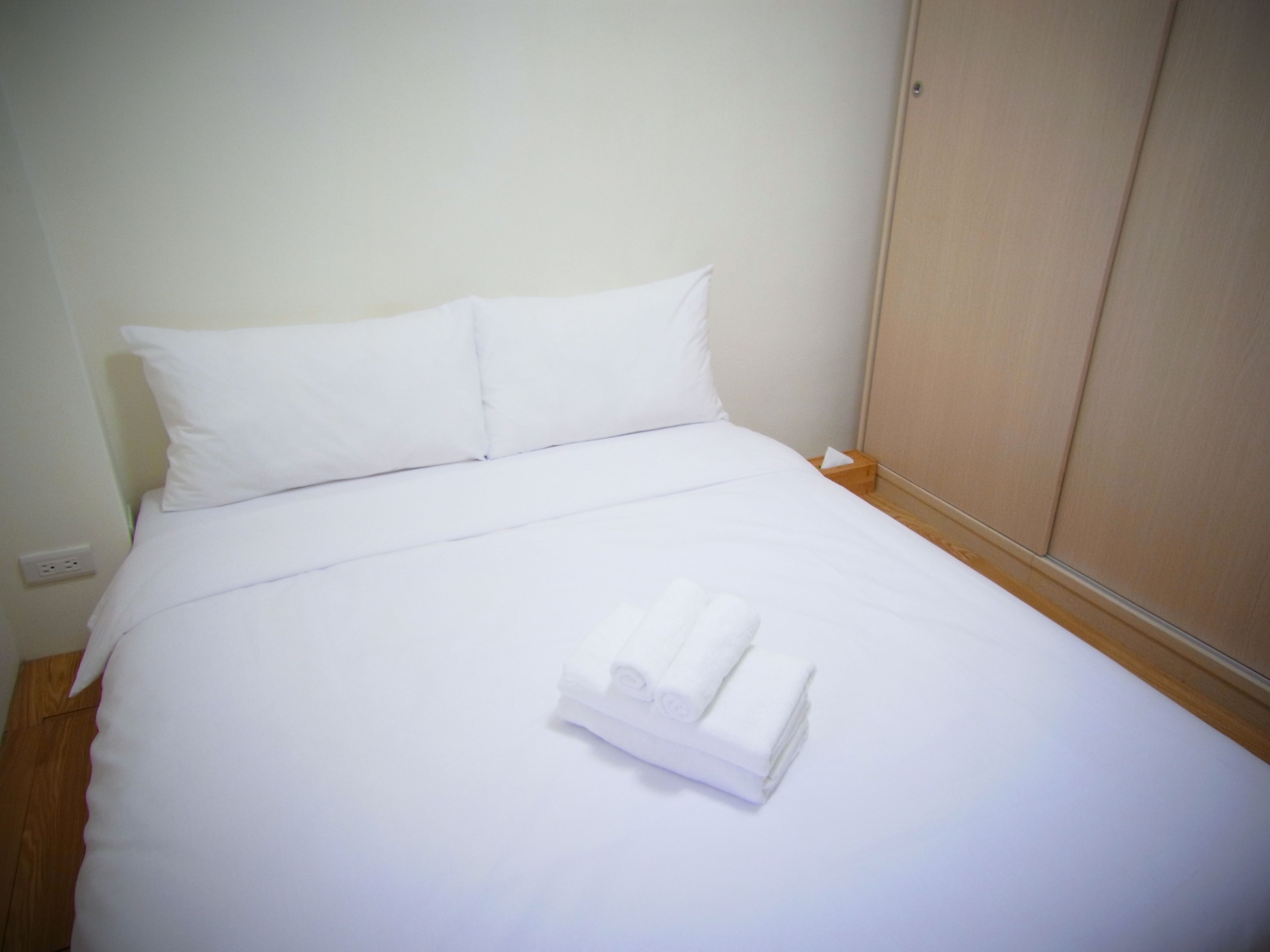 Cama bem arrumada com lençóis brancos e uma toalha dobrada no centro.