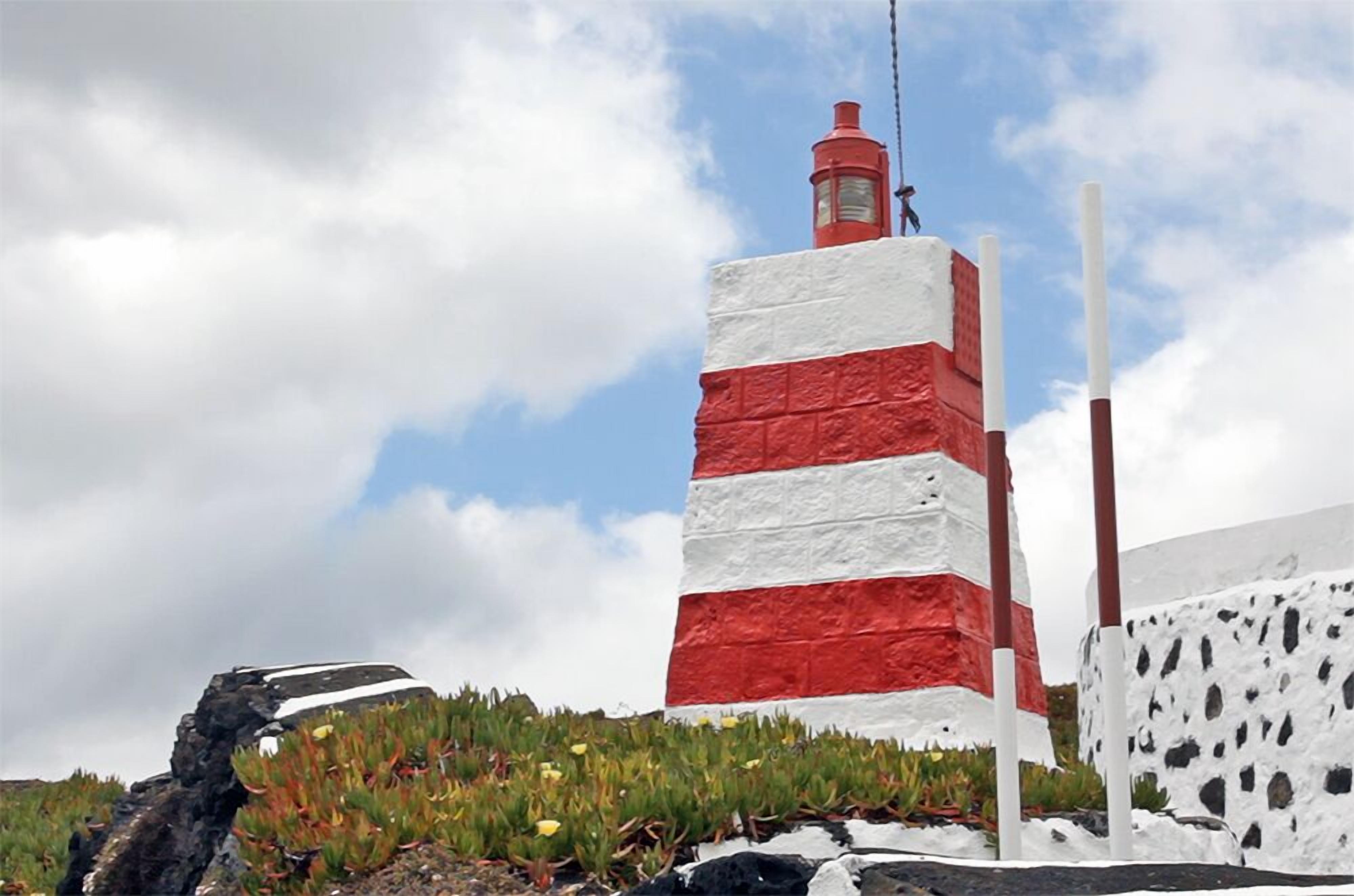 A lighthouse with a red and white striped exterior, situated on a rocky outcrop with sparse vegetation.