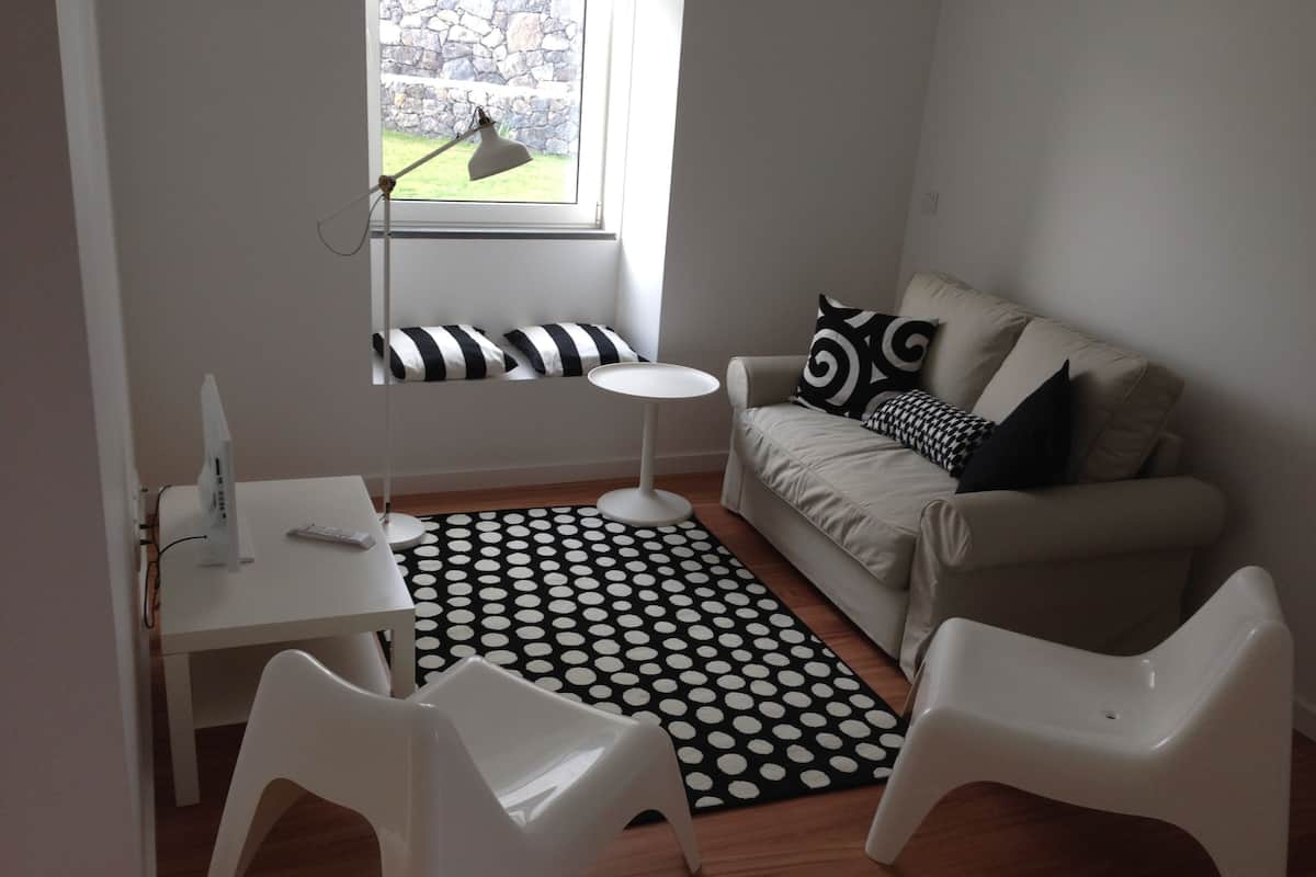 A modern living room with a sofa, a small round table, a white desk, and a polka dot rug.