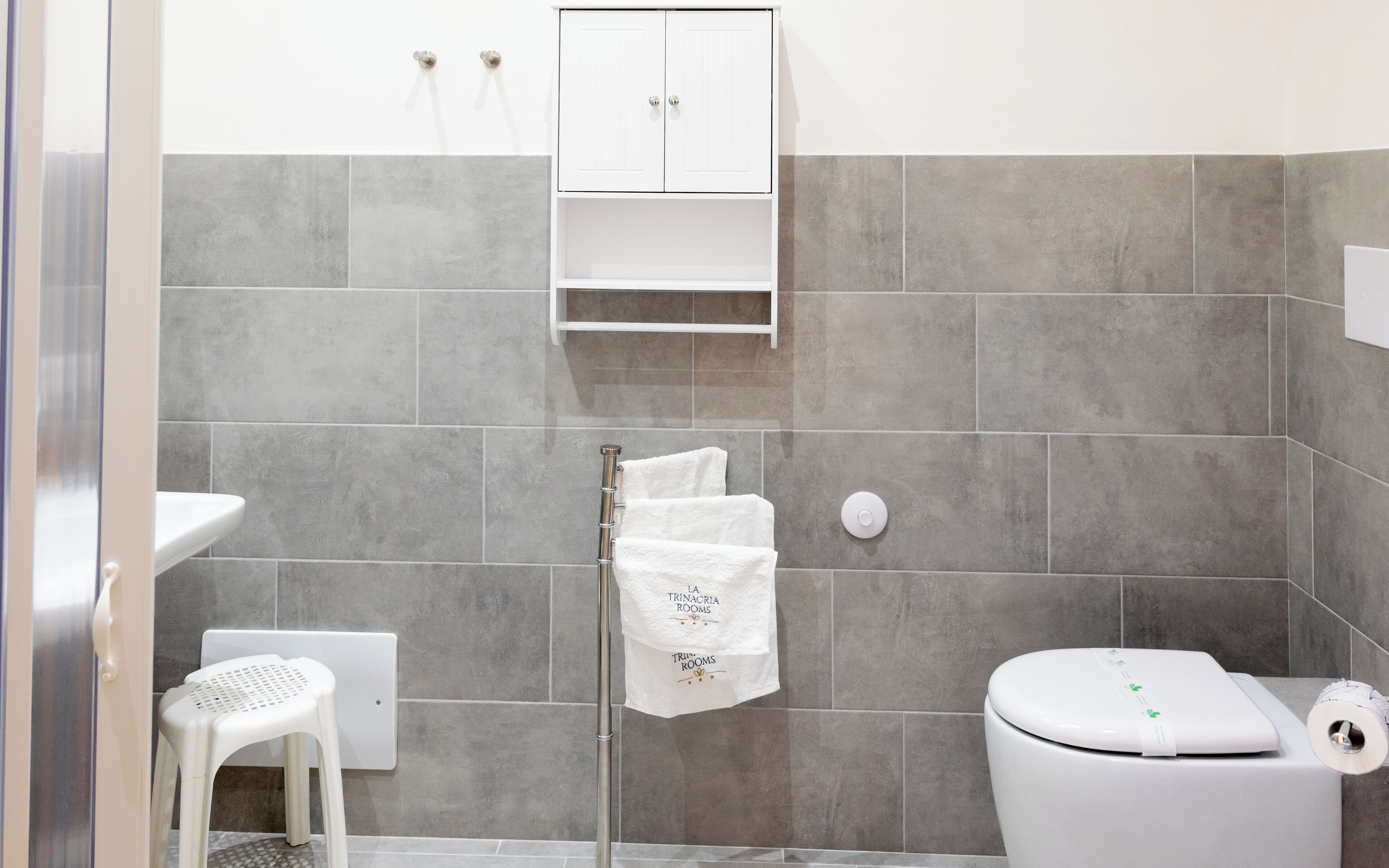 A bathroom with a white toilet, a shower area, and a small white stool.